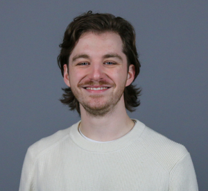 Man with short brown hair wearing a white sweater.