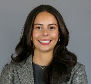 Woman with long, dark brown hair wearing a herringbone blazer.