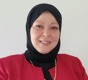 Woman wearing a read blazer over a black top with a pearl necklace and a black headscarf.