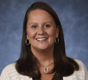 Woman with dark brown hair wearing a white cardigan over a black blouse.