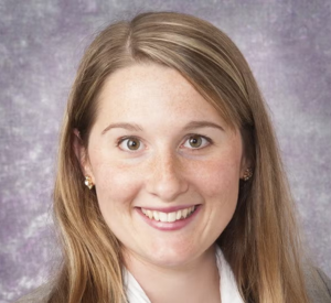 A woman with brown and blonde hair wearing a tan blazer over a white collared shirt.