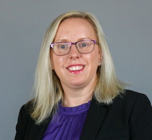 Woman with medium length, blonde hair wearing a purple top and black blazer.