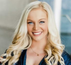 Woman with long, curled blonde hair wearing a dark blue blouse.