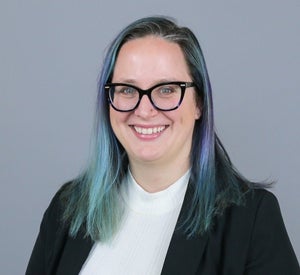 Woman with blue and purple hair wearing bold glasses and a black blazer.