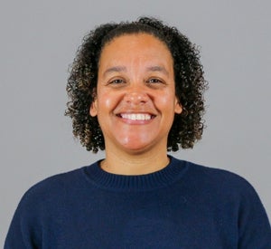 Woman with short, dark brown, curly hair wearing a navy sweater.