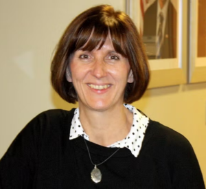 Woman with short brown hair wearing a black sweater over a white collared shirt with black dots.