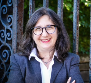 Woman with black hair wearing a dark gray blazer over a white collared shirt.