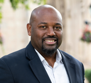 Bald man with a goatee wearing a black suit jacket over a white collared shirt.