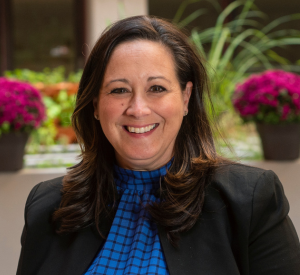 Woman with brown hair wearing a black blazer over a royal blue checkered blouse.