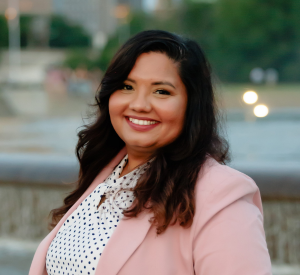 Woman with long brown hair wearing a pink blazer over a black and white polka dot blouse.