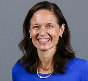 Woman with medium length, dark brown hair, wearing a white necklace and bright blue top.