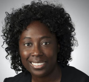 Woman with dark curly hair wearing a black blazer.