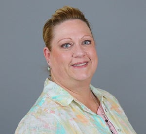 Woman with dark blonde hair pulled back in a ponytail, wearing a pastel colored shirt.