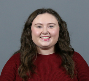 Woman with brown curly hair wearing a dark red sweater.