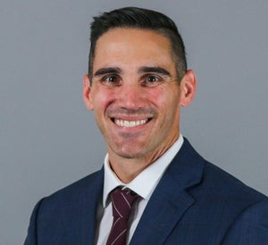 Man with short black hair wearing a dark blue suit and a dark red tie.