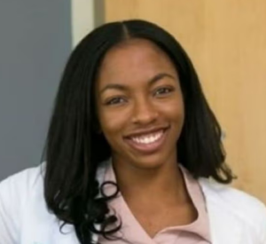 A woman with black hair wearing a white cardigan over a tan shirt.