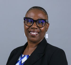 Woman with very short, dark hair wearing bold black glasses, white dangle earrings and a black blazer.