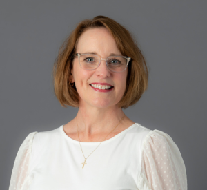 Woman with short auburn hair wearing a white blouse with sheer sleeves with polka dots.