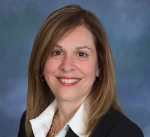 Woman with brown hair wearing a black blazer over a white collared shirt.