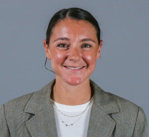 Woman with black hair pulled back into a bun wearing a beige blazer.