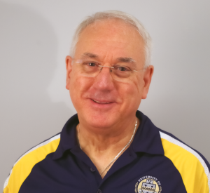 Man with short white hair wearing a dark blue and yellow Pitt polo with silver rimmed glasses and a silver necklace.