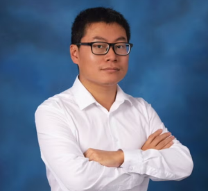 Man with short black hair and glasses wearing a white collared shirt.