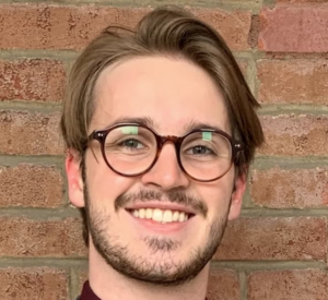 Man with brown hair and glasses wearing a dark red shirt.