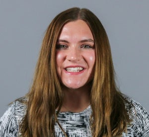 Woman with medium length, brown hair wearing a black and white patterned shirt.