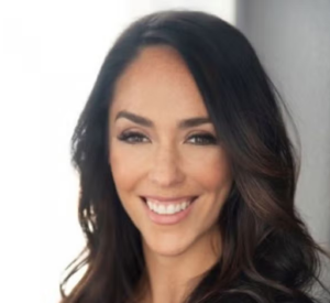 A woman with long brown hair in front of a white and gray background.