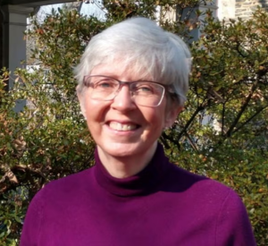 A woman with short white hair wearing a maroon turtleneck.