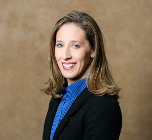 A woman with light brown hair wearing a black blazer over a bright blue blouse.