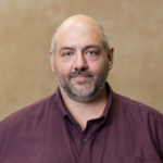 A man with very short gray hair wearing a maroon button-up shirt.