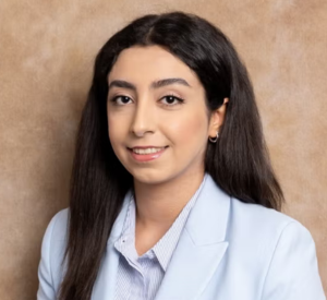 A woman with long, dark brown hair wearing a light blue blazer over a light blue collared shirt.