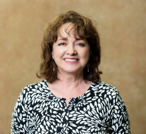 A woman with brown curly hair wearing a black blouse with a white floral print.