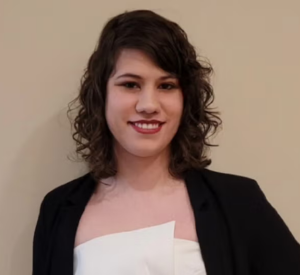 Woman with short curly hair wearing a black cardigan over a white strapless shirt.