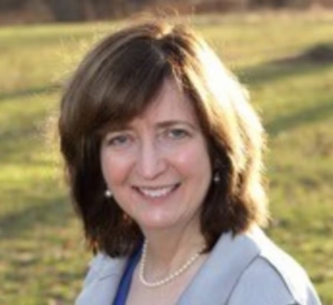 Woman with brown hair wearing a gray blazer over a dark blue shirt with a pearl necklace.