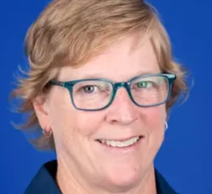 Woman with short, dark blonde hair wearing a navy blue collared shirt and blue glasses.