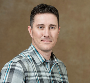 A man with short black hair wearing a green plaid shirt.