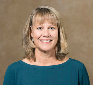 Woman with short blonde hair wearing a dark green blouse.