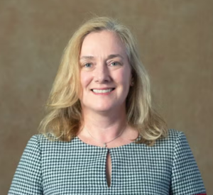 Woman with blonde hair wearing a green and white checkered blouse.