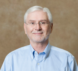 A man with white hair wearing a light blue collared shirt.