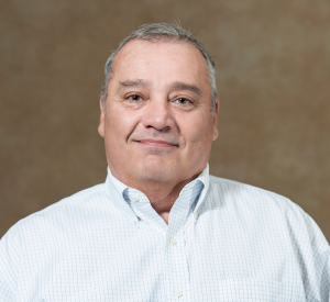 A man with short gray hair wearing a white collared shirt with small gray lines