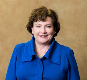 A woman with short brown hair wearing a royal blue collared blouse.