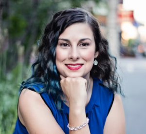 Woman with curly, dark brown hair with dyed blue strands wearing a sleeveless royal blue top.