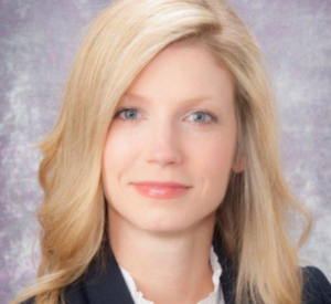 Woman with long blonde hair wearing a black blazer over a white blouse.