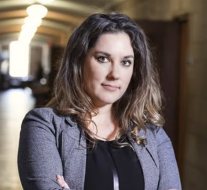 Woman with brown hair wearing a gray blazer over a black blouse.