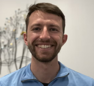 Man with short brown hair wearing a light blue collared shirt.