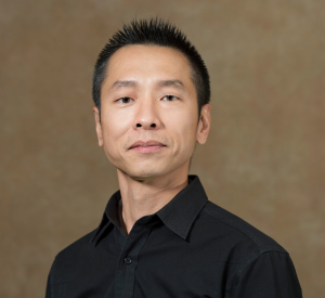 A man with black hair wearing a black collared shirt.