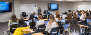 Full classroom photo from the back of the classroom observing a speaker.