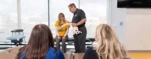 Students watching an male instructor and female student at the front of a classroom with a spine model.